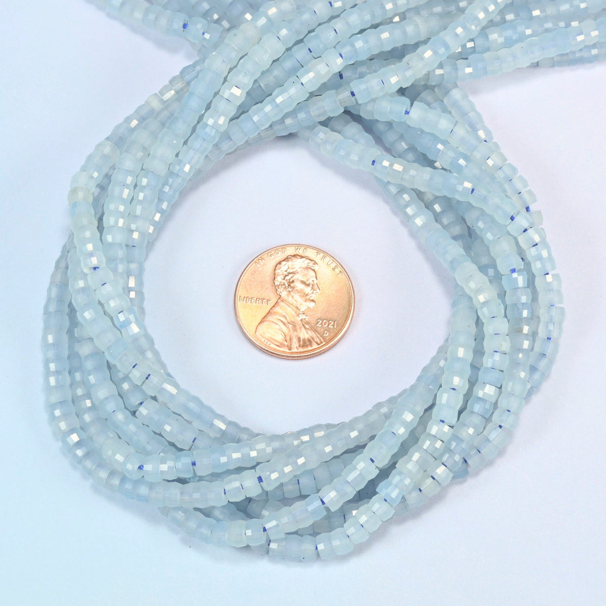Aquamarine chalcedony faceted heishi disc beads 2x4mm coiled in a loop around a US penny for scale, close-up of the faceted disc shape