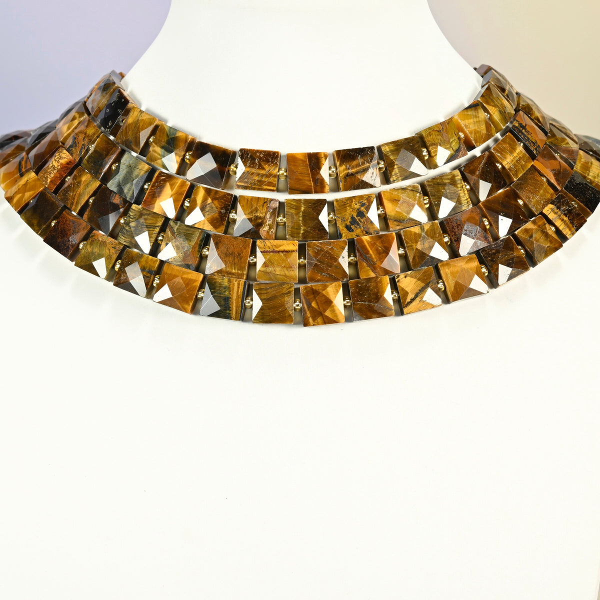 Natural tiger eye faceted flat square strands arranged as a layered collar on a white display bust, golden brown beads across the neck