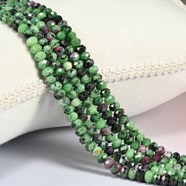 Ruby Zoisite gemstone rondelle beads 4x6mm faceted, strand draped over a cream fabric cushion