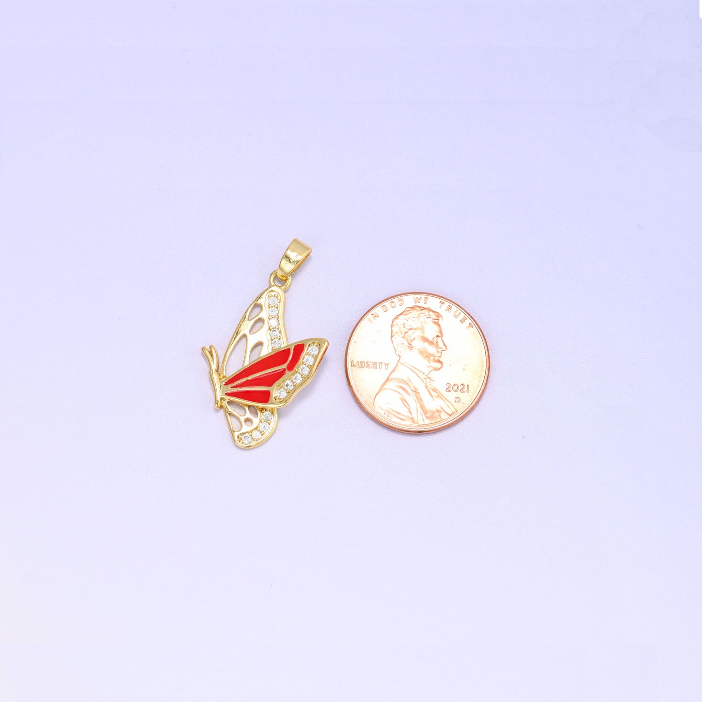 Scale shot of the flying butterfly charm pendant, the red enamel butterfly beside a US penny and a little taller than the coin.
