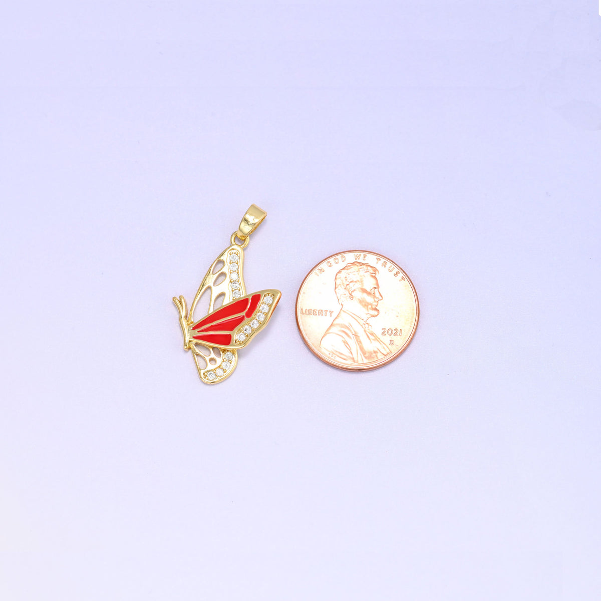 Scale shot of the flying butterfly charm pendant, the red enamel butterfly beside a US penny and a little taller than the coin.