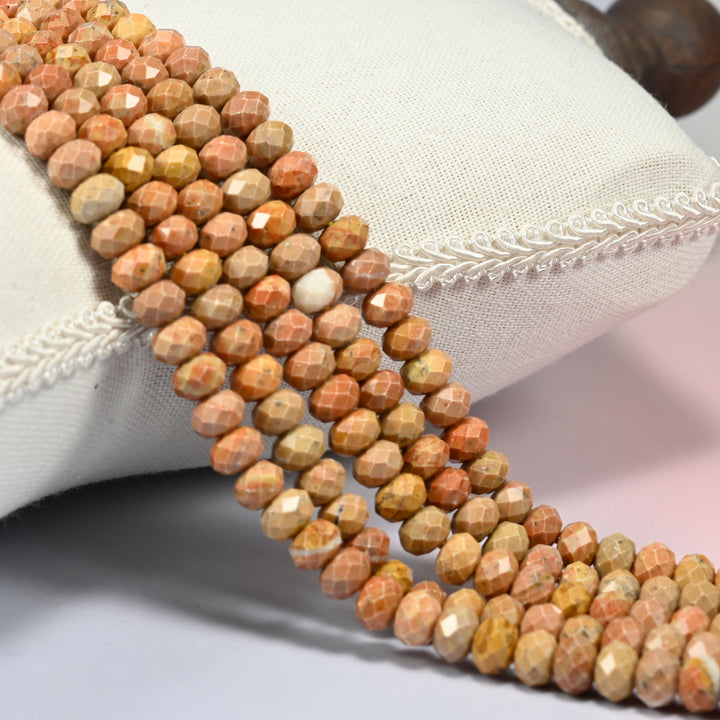 Orange stone faceted rondelle beads 5x8mm in warm peach orange and tan, several strands draped over a white cushion