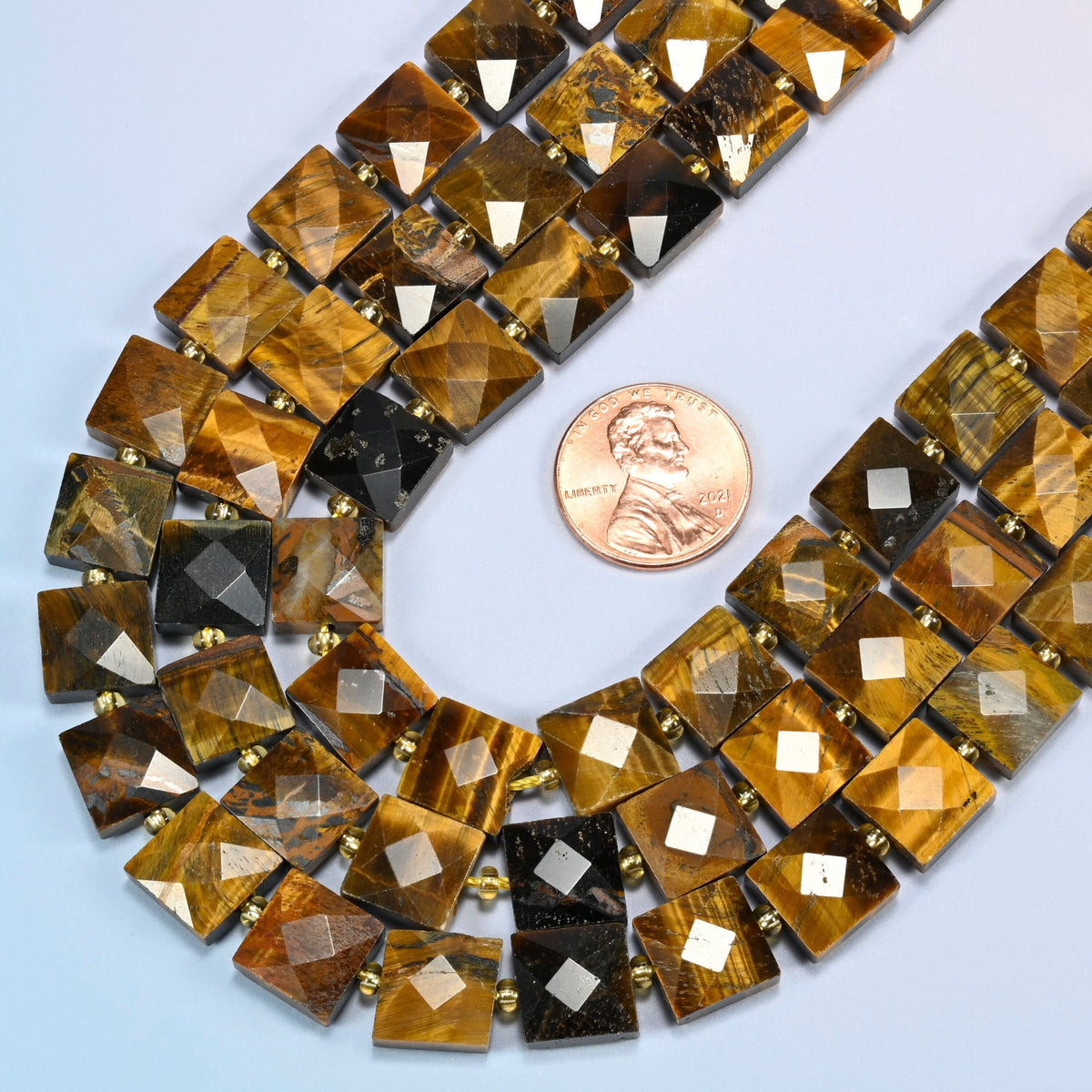 Close view of natural tiger eye faceted flat square strands curving beside a US penny for scale