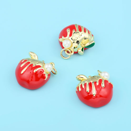 A domed half apple in glossy pillar-box red enamel with a white icing drip down one side, a gold stem and leaf, a small…