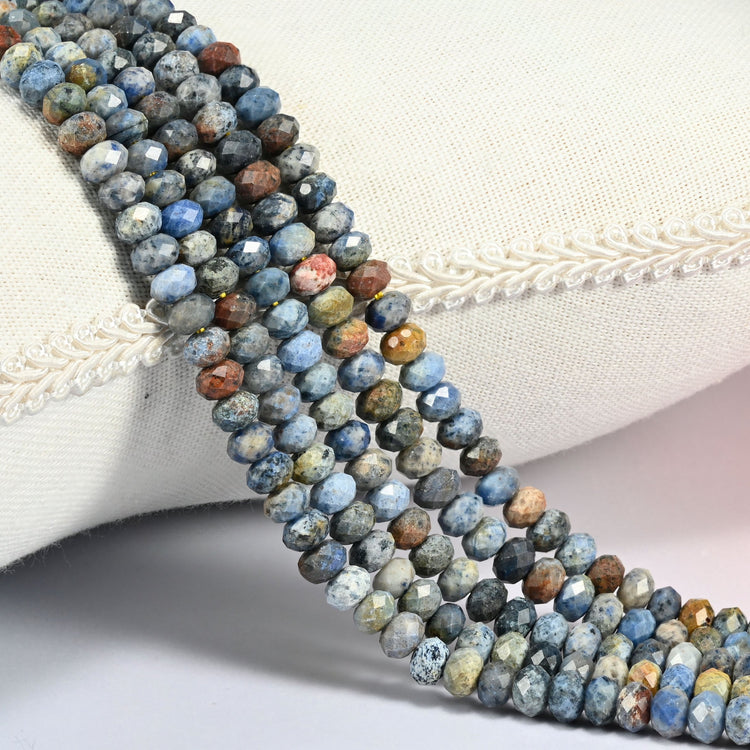 Sunset Dumortierite gemstone rondelle beads 4x6mm faceted, strand draped over a cream fabric cushion