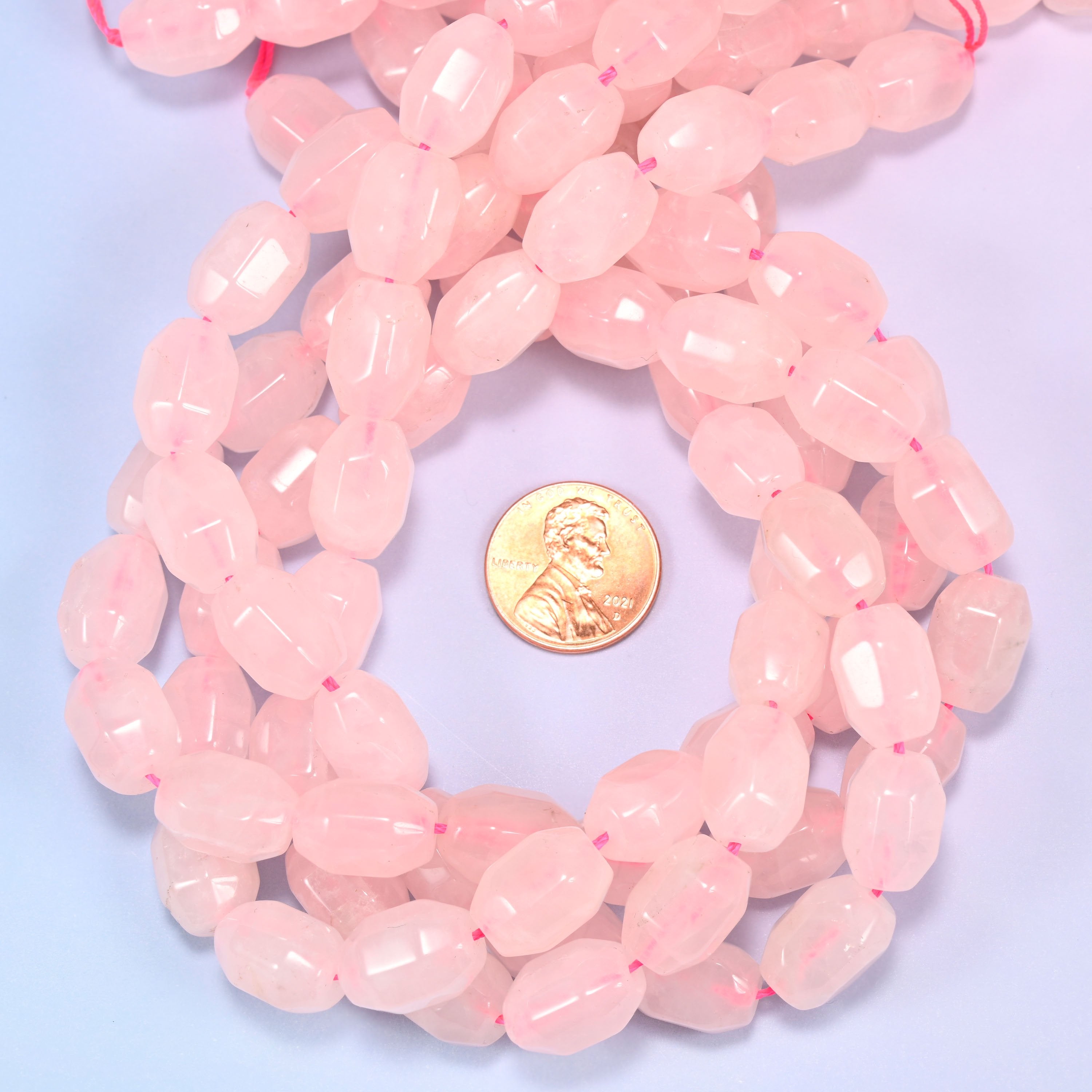 Close-up circular coil of Rose Quartz faceted barrel bead strands with a penny in the center for size comparison.