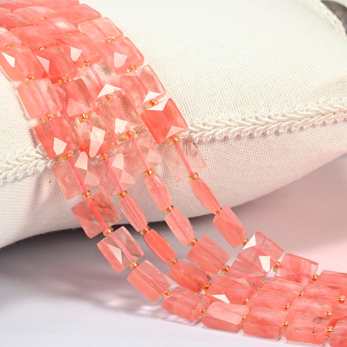 Melon quartz faceted flat square beads 10x10mm with small gold seed bead spacers, several strands draped over a white cushion