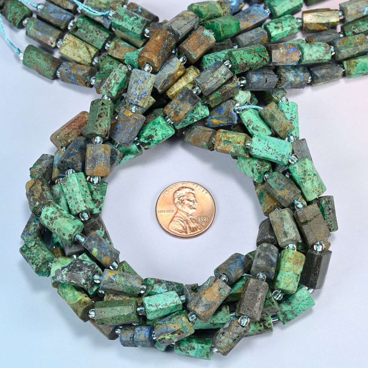 Azurite chrysocolla faceted tube beads 9x7-12x8mm coiled in a loop around a US penny for scale, close-up of the faceted tube shape