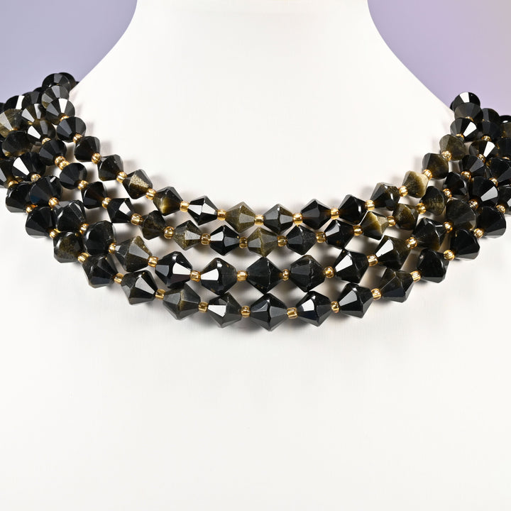 Gold obsidian bicone beads curved into a collar, the golden shimmer lifting on the beads that catch the light and disappearing on the rest.