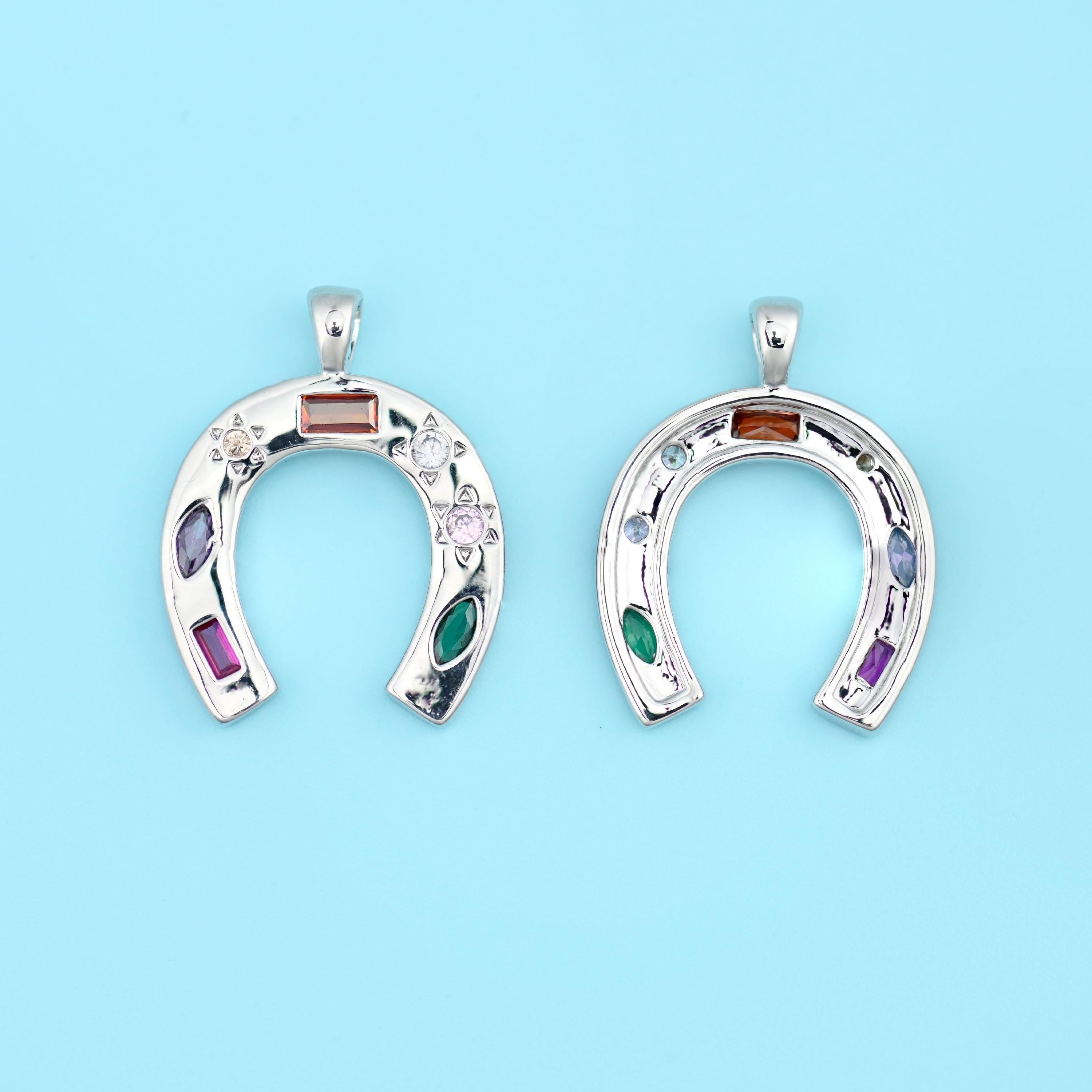A horseshoe pendant set with coloured zircon stones in amber, deep purple, emerald green and rose, scattered between tiny…