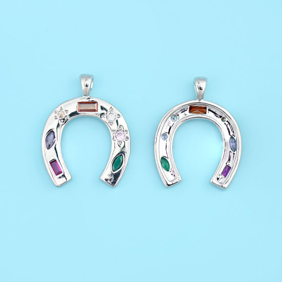 A horseshoe pendant set with coloured zircon stones in amber, deep purple, emerald green and rose, scattered between tiny…