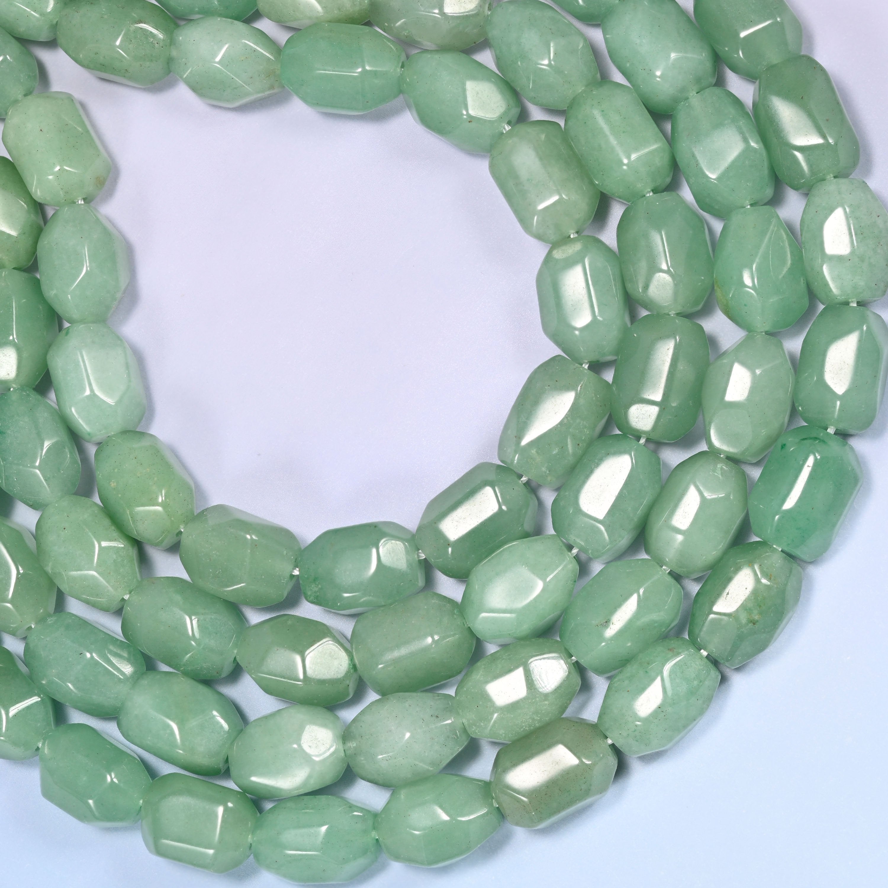 Circular coil of green faceted Aventurine barrel bead strands on a light lavender background with a penny in the center for size comparison.