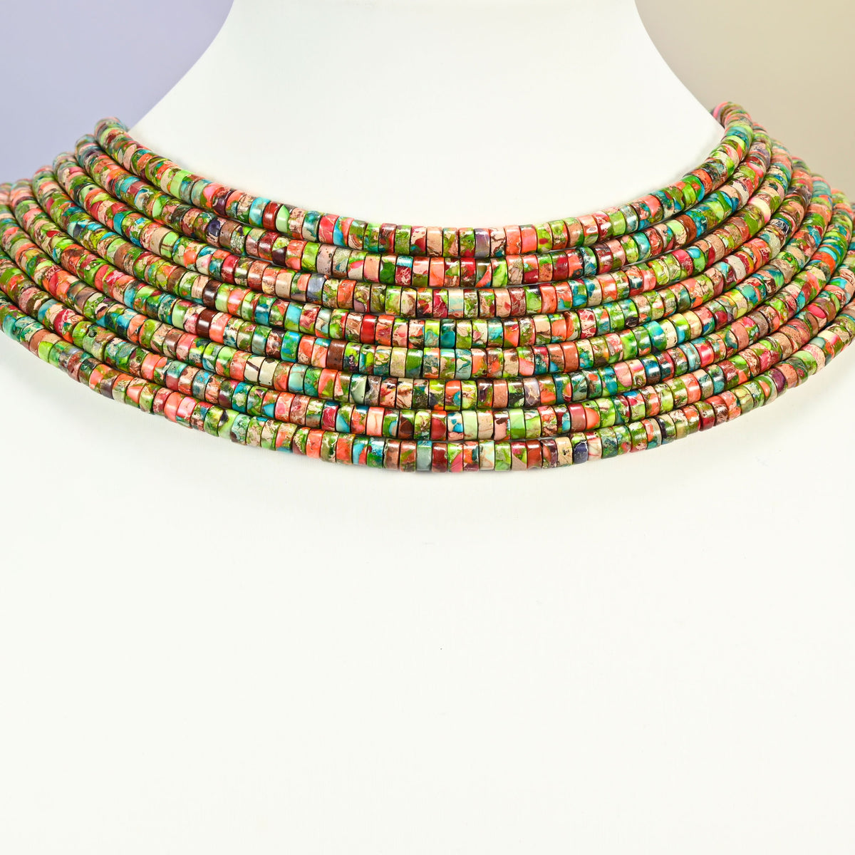 Dyed blue green sea sediment jasper heishi disc strands arranged as a layered collar on a white display bust