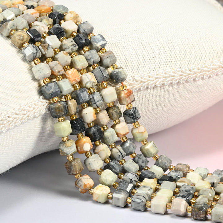 Picasso jasper faceted cube beads 6mm with small gold spacer beads, several strands draped over a white cushion