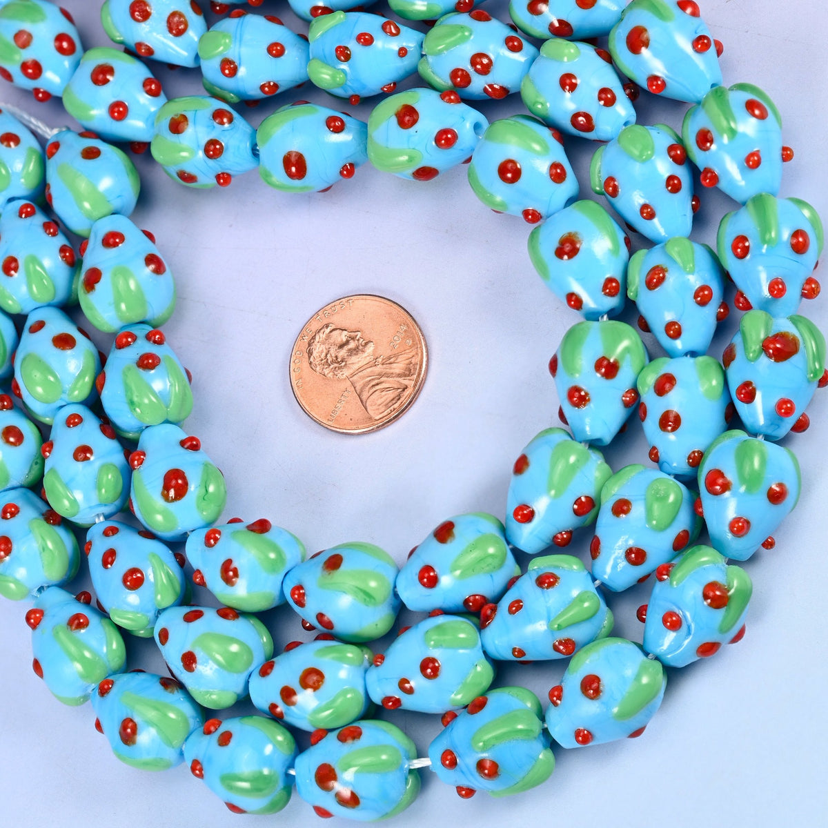 A plump moulded berry in glossy sky blue, capped with a green glass leaf and scattered with small red dots for seeds.