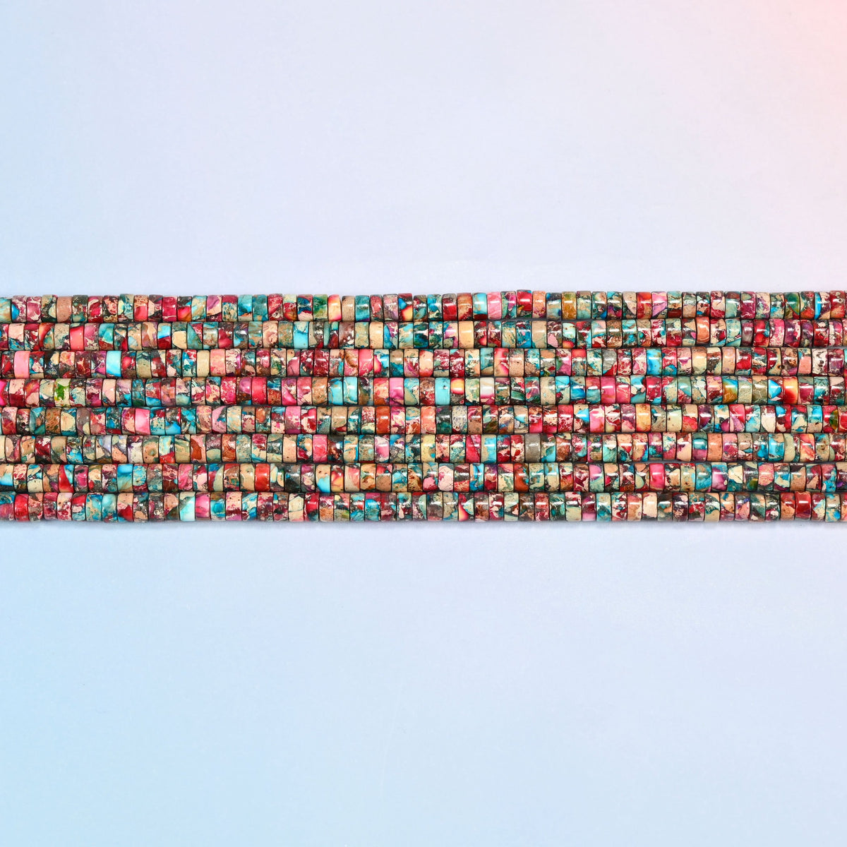 Several strands of dyed pink blue sea sediment jasper heishi disc beads 2x4mm laid in straight rows, pink and turquoise discs side by side