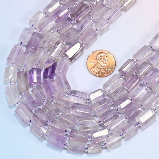 Lavender amethyst faceted tube beads coiled in a loop with a US penny resting at the right edge for scale.