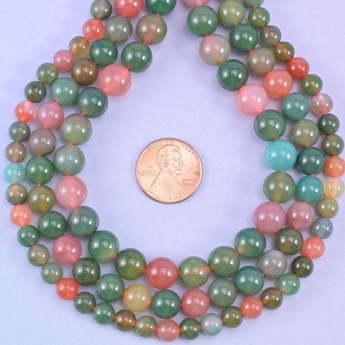Green Yanyuan Agate smooth round beads coiled around a US penny for size reference, approximately 45 beads on a 14 inch strand at 8mm
