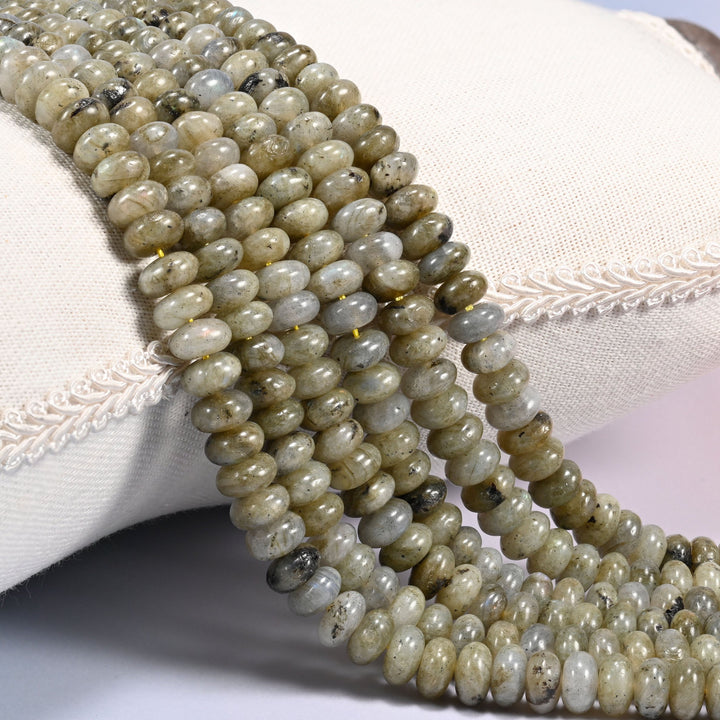 Close-up of multiple strands of polished Grey Labradorite rondelle beads draped over a cream fabric jewelry display bust.
