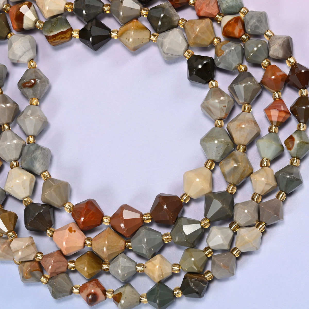 American Picture Jasper faceted bicone beads, 8mm and 10mm, coiled into a loose circle on a light lavender background.