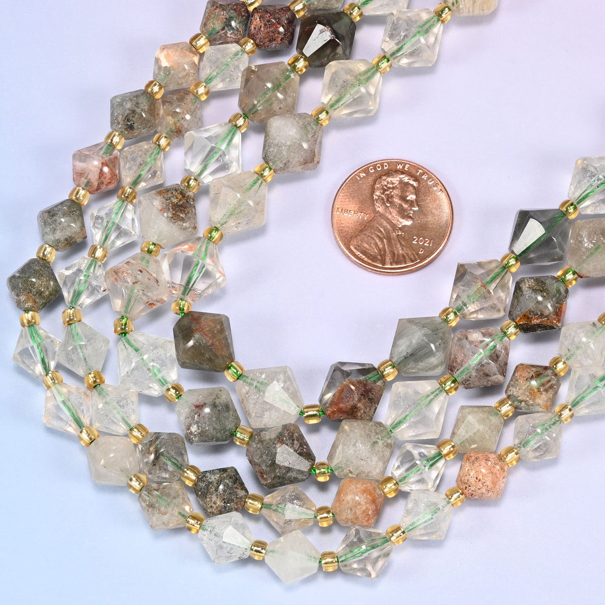 Close-up of Green Phantom Quartz faceted bicone beads, 8mm and 10mm, in a loose curved strand, showing the faceted cut and natural color variation.