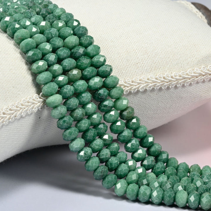 Natural green jade faceted rondelle beads 5x8mm in mottled forest green and sage, several strands draped over a white cushion