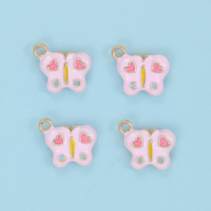 Enamel butterfly charm in soft pink, shown as four charms with deeper pink hearts, blue dots and gold jump rings set above the head.