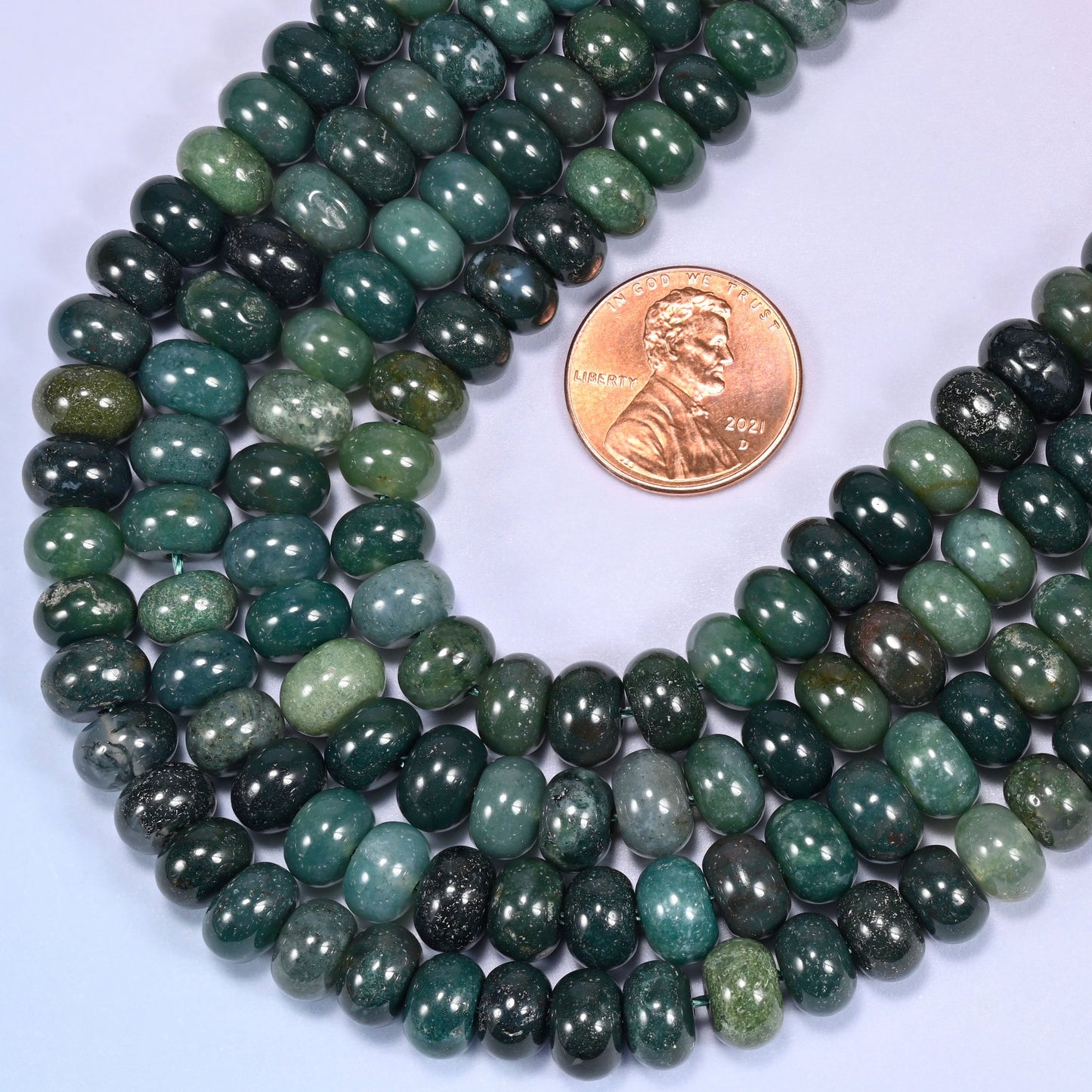 Circular coil of Moss Agate bead strands on a lavender background with a penny in the center for size comparison.