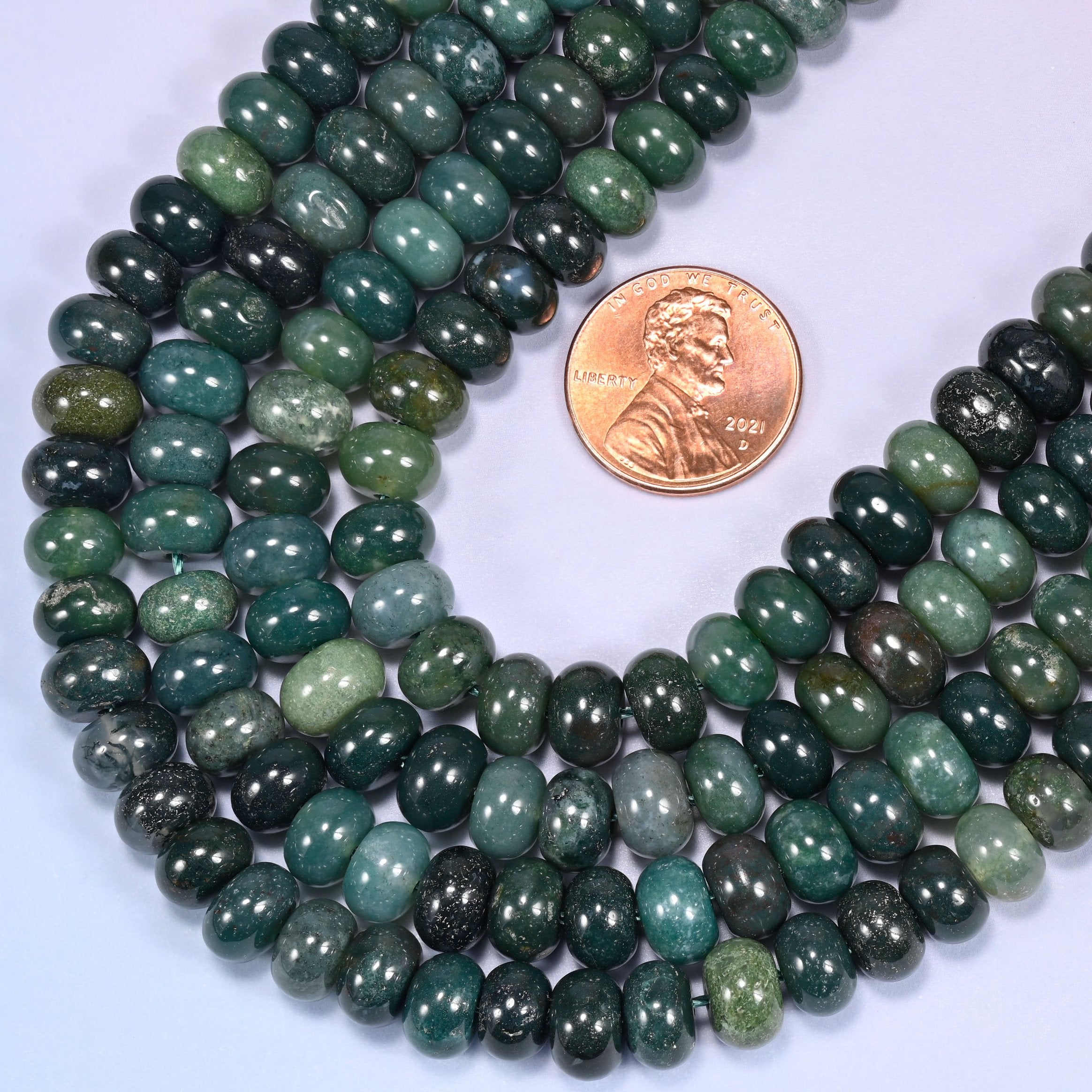 Circular coil of Moss Agate bead strands on a lavender background with a penny in the center for size comparison.