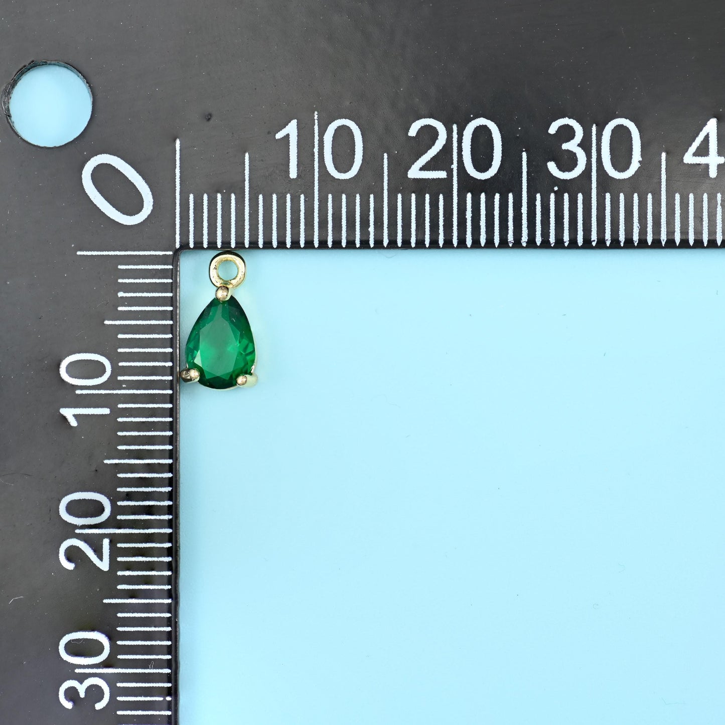 Teardrop zirconia charm in green on a black millimetre ruler, about 10mm long.