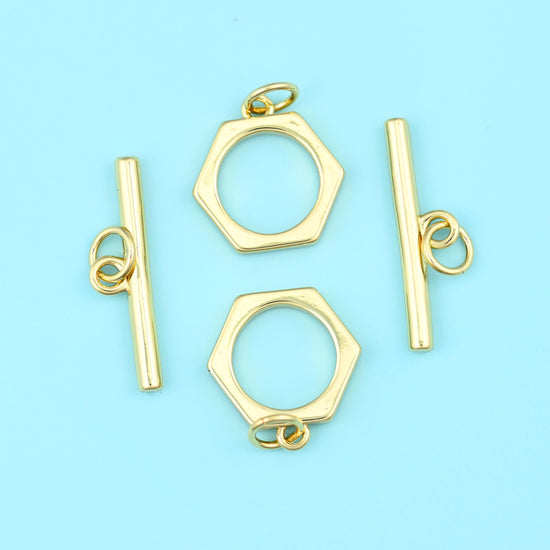 A crisp six-sided ring paired with a smooth straight bar, both carrying a warm satin 18K gold filled finish over brass, and…