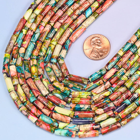Coiled strands of multicolor jasper tube beads on a lavender surface with a US penny placed beside them for scale reference.