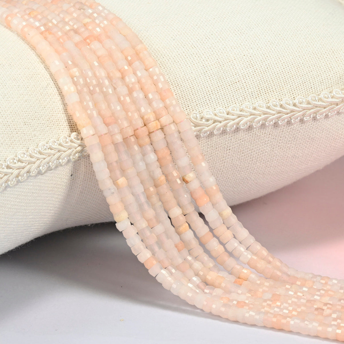 Pink aventurine faceted heishi disc beads 2x4mm, several strands draped over a white cushion