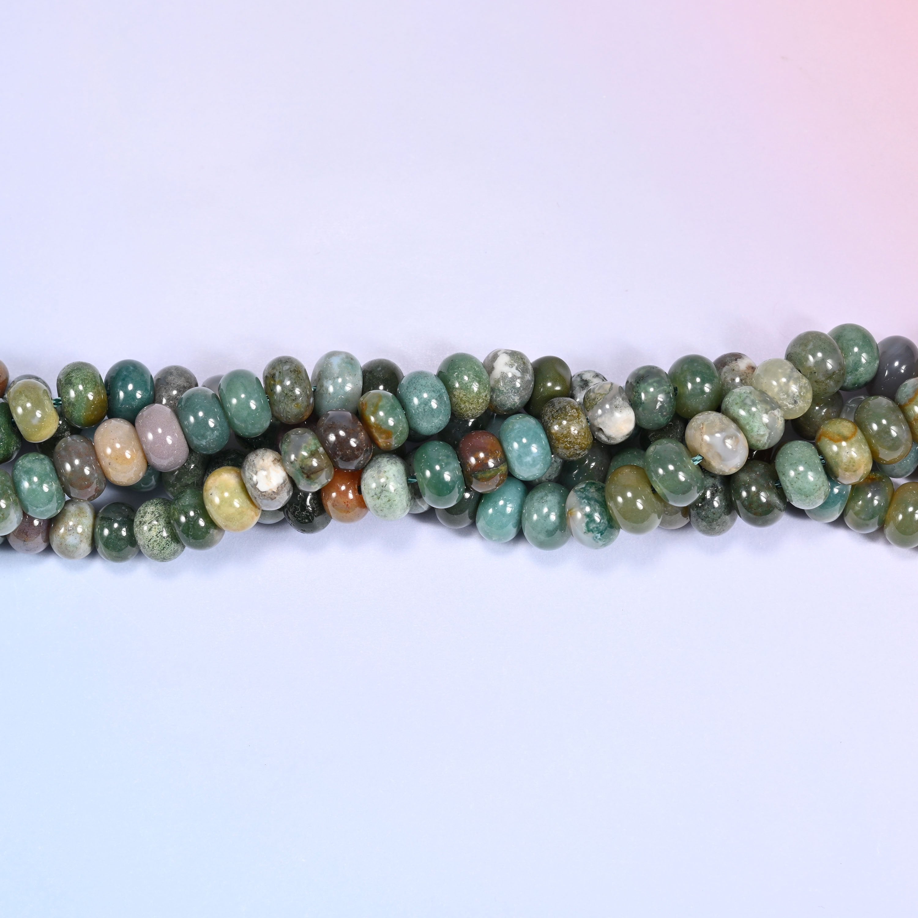 Bundled coil of Indian Agate rondelle beads on a lavender background with a penny placed at the center for scale.