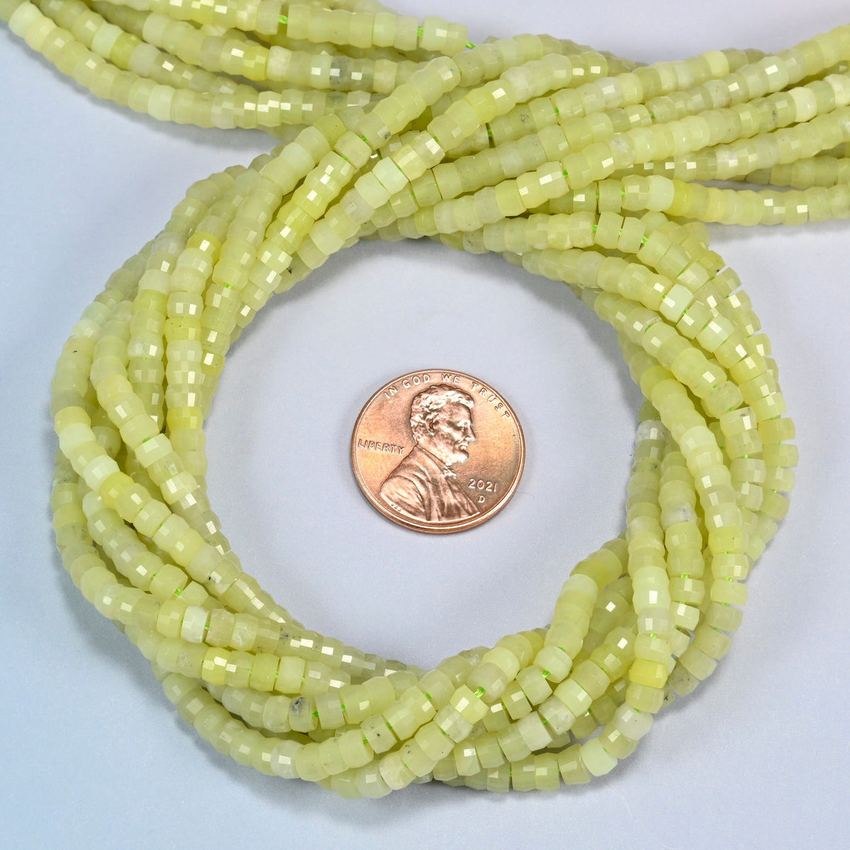 Lemon Jade faceted heishi disc beads 2x4mm coiled in a loop around a US penny for scale, close-up of the faceted disc shape