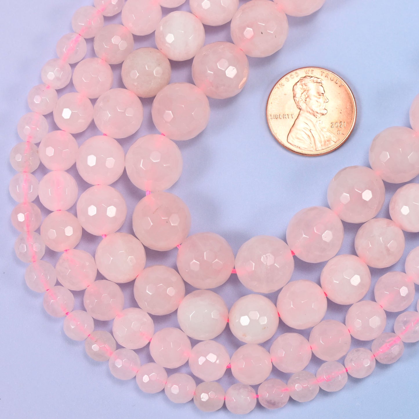 Pink rose quartz round beads in 6mm, 8mm, 10mm, and 12mm grouped together to compare sizes.