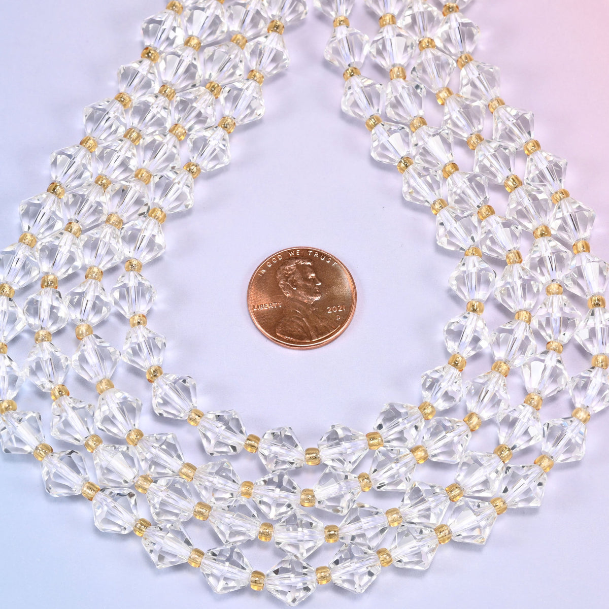Close-up of 8mm Clear Quartz faceted bicone beads arranged in a loose curved loop, showing the transparent sparkle of the strand.