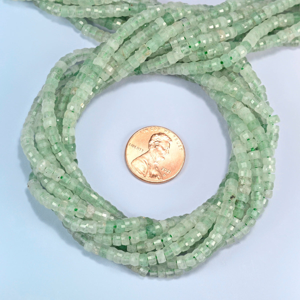 Green strawberry quartz faceted heishi disc beads 2x4mm coiled in a loop around a US penny for scale, close-up of the faceted disc shape