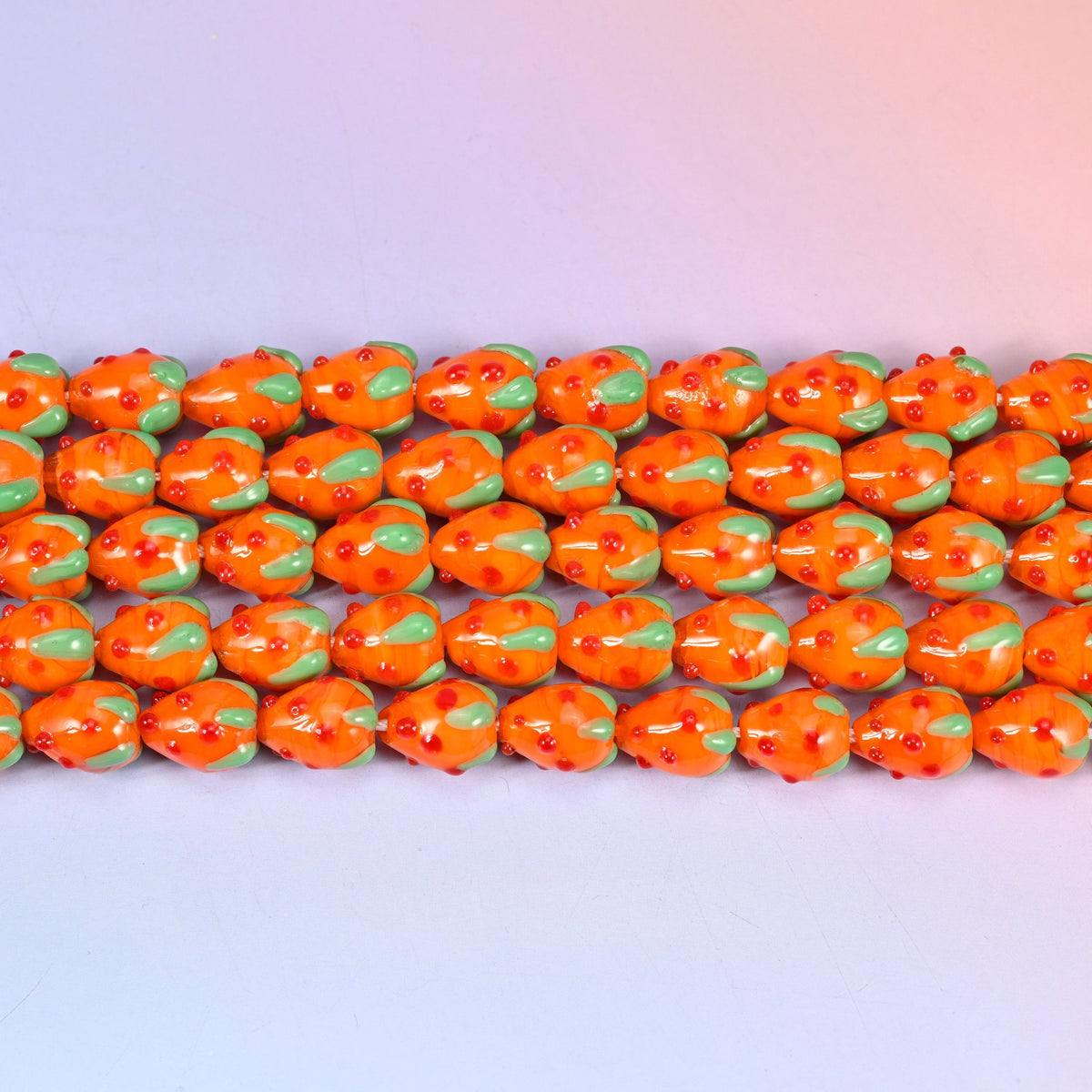 Glossy tangerine orange strawberry glass beads with red seed dots and a green leaf cap