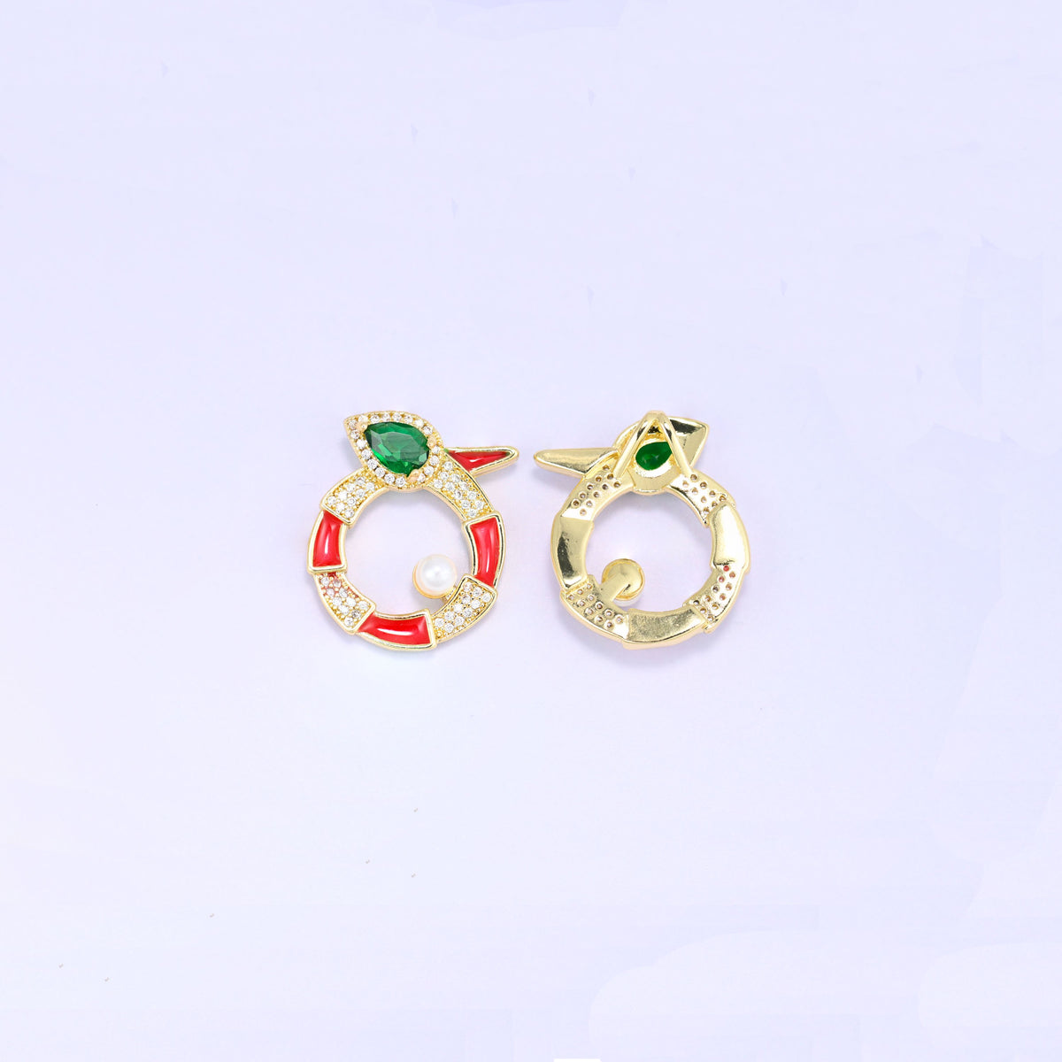 Round snake charm shown front and back, the red enamel and zircon face beside the plain gold reverse of a second piece, both standing upright.