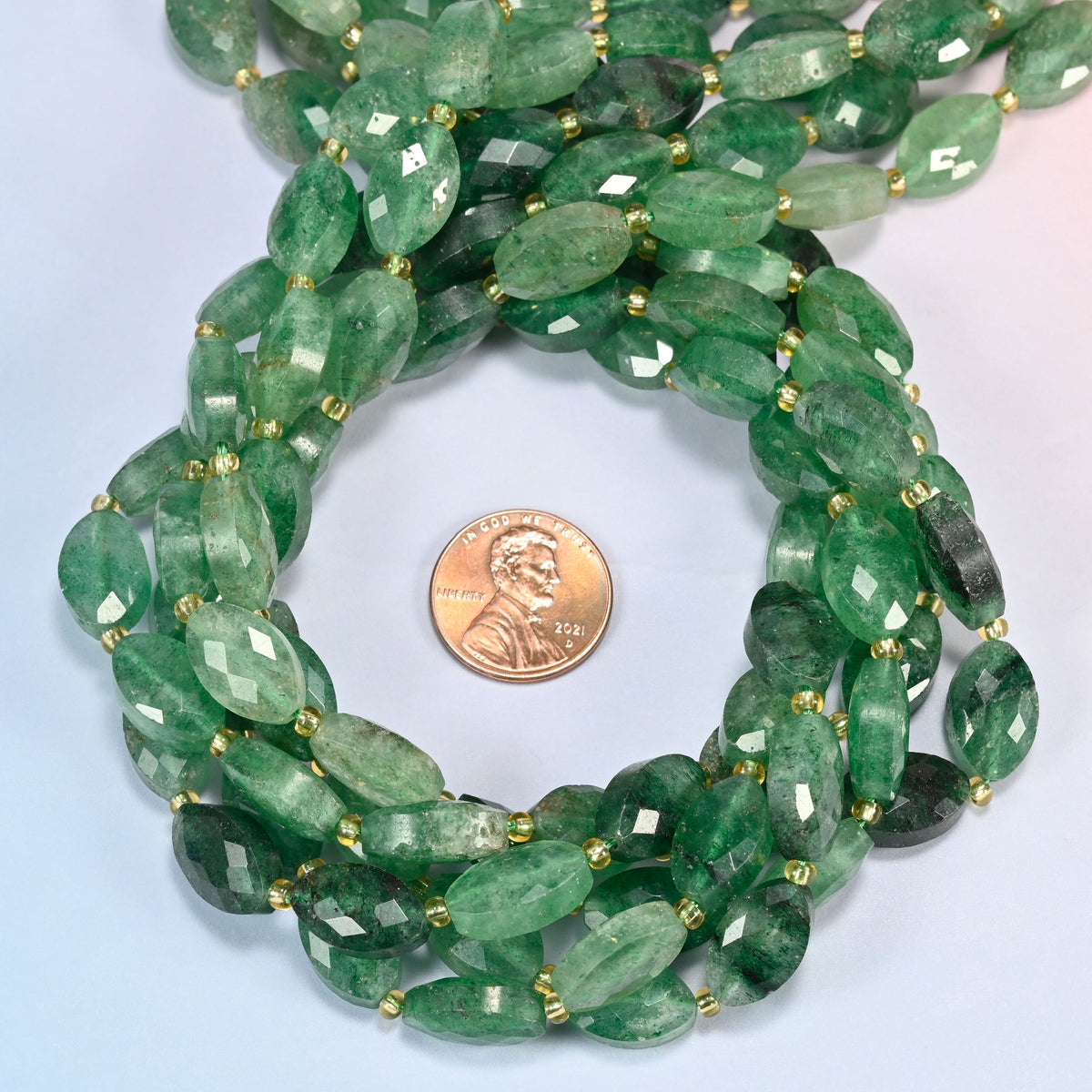 Green strawberry quartz faceted flat oval beads 9x14mm coiled in a loop around a US penny for scale, close-up of the faceted flat oval shape