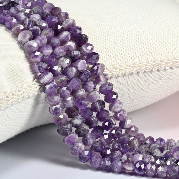 Chevron amethyst faceted rondelle beads in violet striped with milky white, three strands draped over a linen cushion