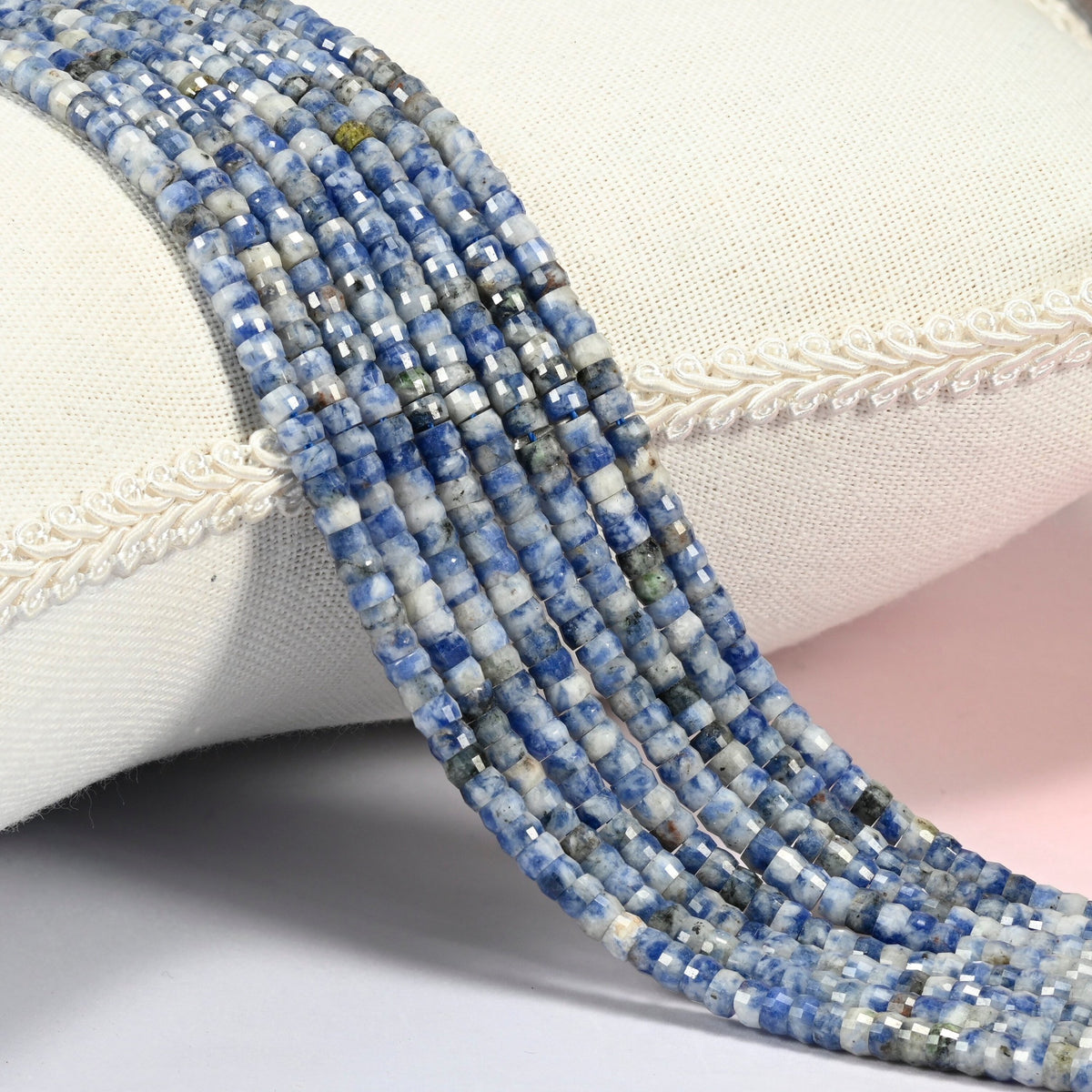Blue spot jasper faceted heishi disc beads 2x4mm, several strands draped over a white cushion
