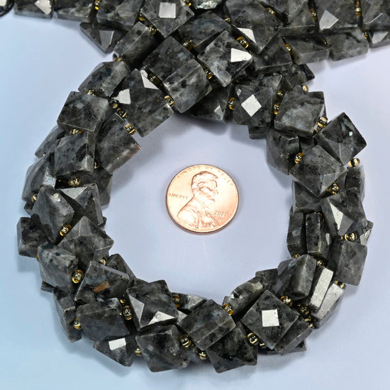 Natural black labradorite faceted flat square beads 10x10mm coiled in a loop around a US penny for scale, close-up of the faceted flat square shape