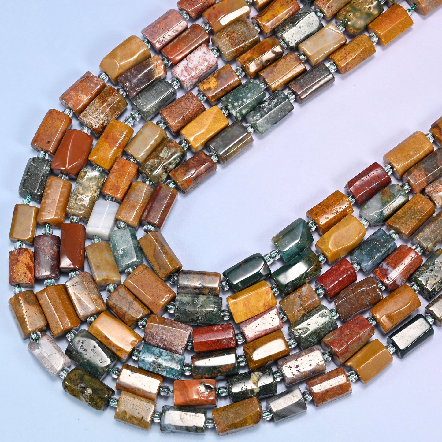 Close-up of faceted Ocean Jasper tube beads with clear glass spacer beads on a lavender background.