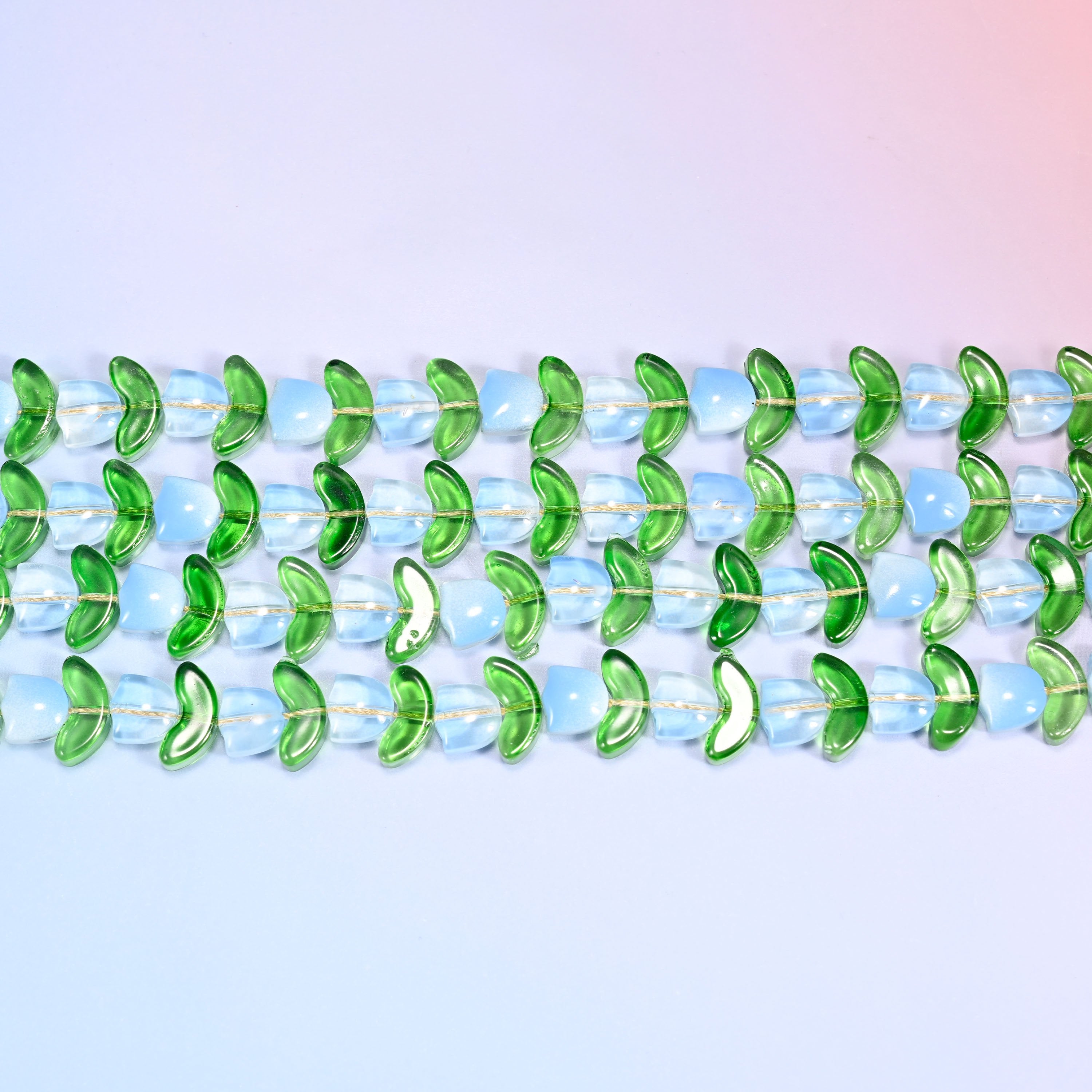 Close-up macro view of light blue tulip and green leaf glass beads in a dense repeating chevron pattern on a lavender and pink gradient background.