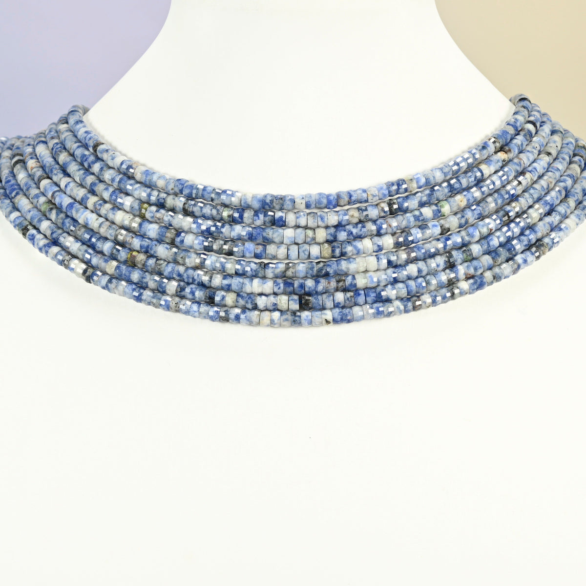 Blue spot jasper faceted heishi disc strands arranged as a layered collar on a white display bust, blue and white beads across the neck
