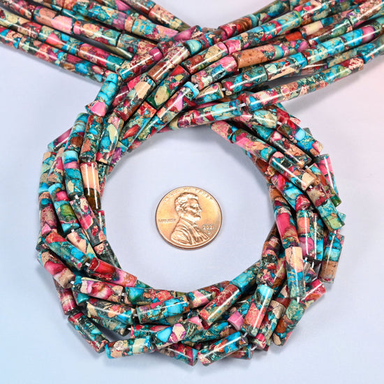 Dyed sea sediment jasper tube beads 13x4mm coiled in a loop around a US penny for scale, close-up of the slim tube shape