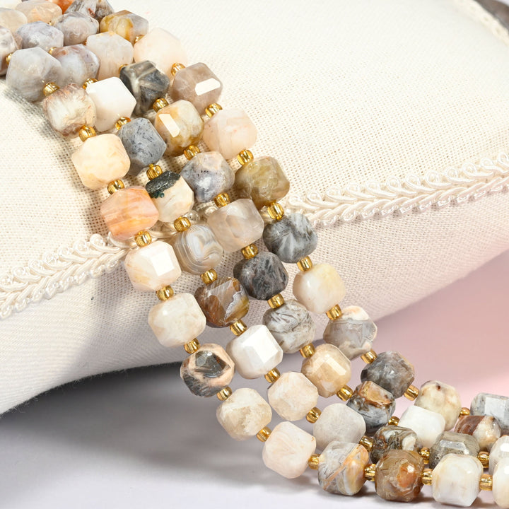 Bamboo agate faceted cube beads 8mm with small gold spacer beads, several strands draped over a white cushion