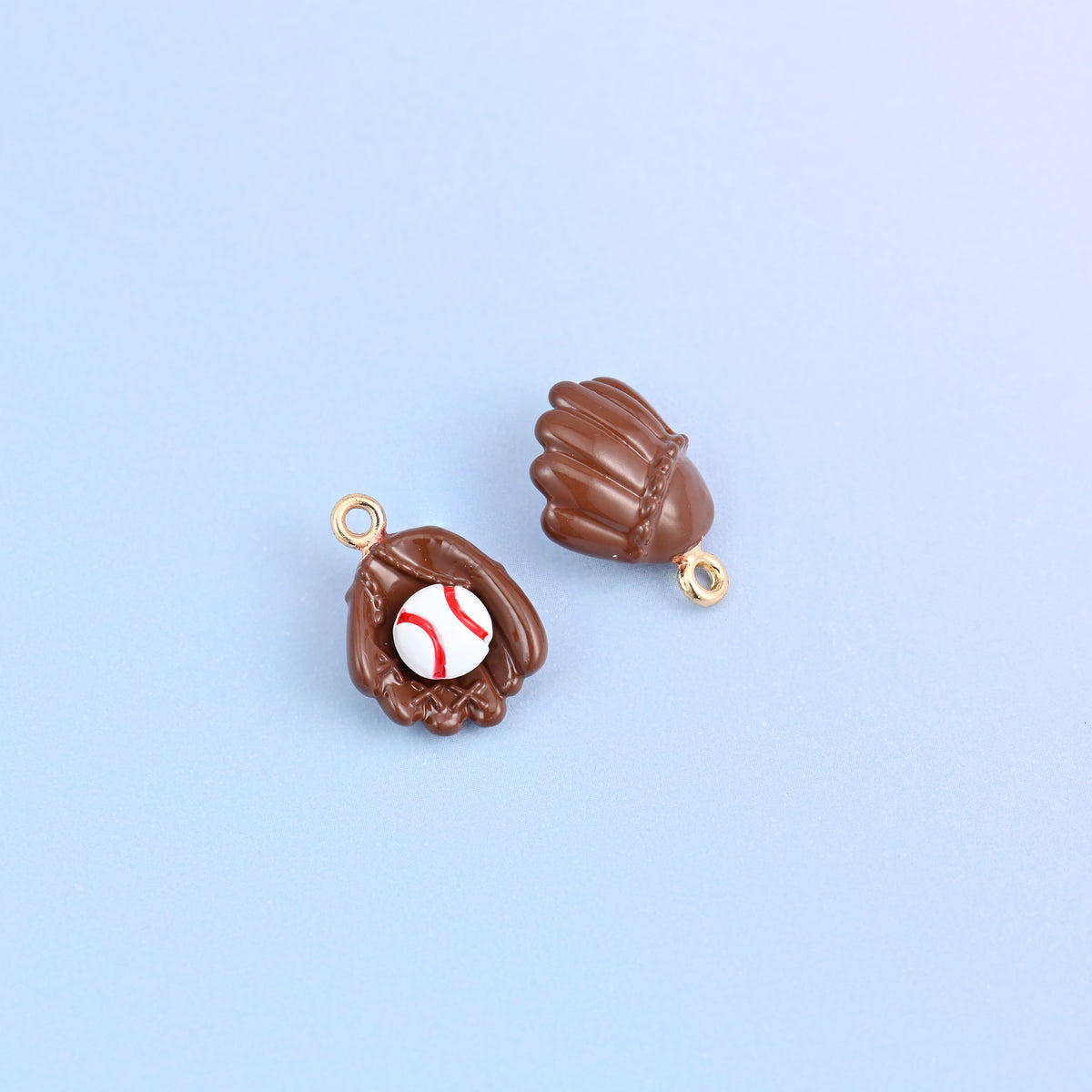 Two brown baseball glove charms, front and back, the ball sitting in the pocket with red stitching painted on.
